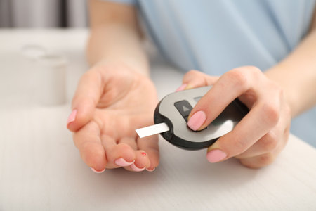 Diabetes. Woman checking blood sugar level with glucometer at wooden table, closeupの写真素材