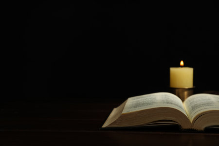 Church candle and Bible on wooden table against black background, space for textの写真素材