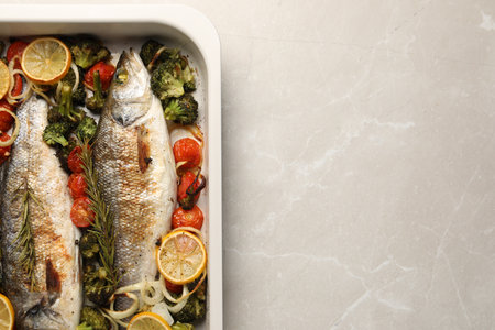 Delicious fish with vegetables and lemon in baking dish on light marble table, top view. Space for textの写真素材