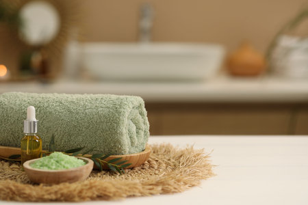 Spa composition. Rolled towel, cosmetic product, sea salt and twig on table indoors. Space for textの写真素材