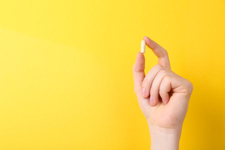Woman holding vitamin capsule on yellow background, closeup. Space for textの写真素材