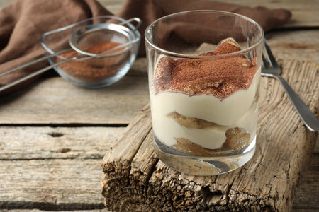 Delicious tiramisu in glass and fork on wooden table, closeup. Space for textの写真素材