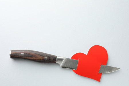 Broken heart. Red paper heart pierced with knife on white background, top view. Space for textの写真素材