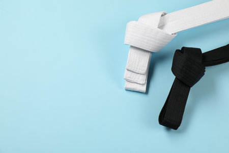 White and black karate belts on light blue background, flat lay. Space for textの写真素材