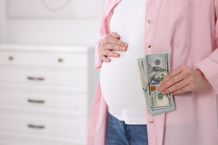 Surrogate mother. Pregnant woman with dollar banknotes indoors, closeup. Space for textの写真素材