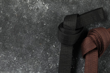 Black and brown karate belts on gray textured background, flat lay. Space for textの写真素材