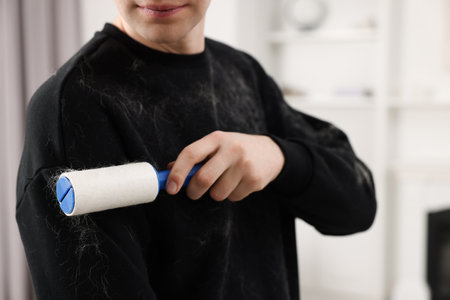 Pet shedding. Man with lint roller removing dog's hair from sweater at home, closeupの写真素材