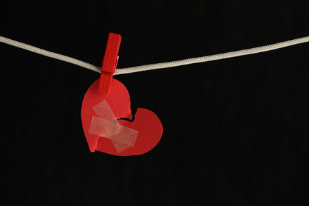 Broken heart. Torn red paper heart with medical adhesive bandages on black background, space for textの写真素材