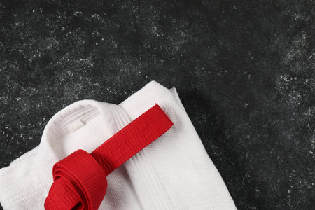 Red karate belt and white kimono on gray textured background, top view. Space for textの写真素材
