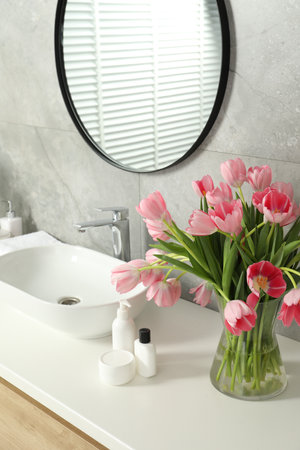 Vase with beautiful pink tulips and toiletries near sink in bathroomの写真素材