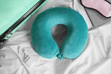 Turquoise travel pillow, suitcase, sleep mask and earphones on bed, flat layの写真素材