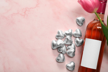 Delicious heart shaped chocolate candies, beautiful tulip and bottle of wine on pink table, flat lay. Space for textの写真素材
