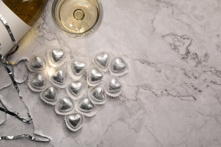 Heart made with delicious chocolate candies and champagne on white marble table, flat lay. Space for textの写真素材