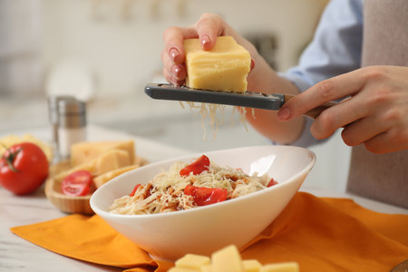 Woman grating cheese onto delicious pasta at white marble table in kitchen, closeupの写真素材
