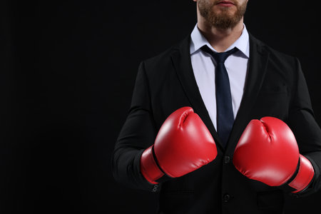 Businessman in suit wearing boxing gloves on black background, closeup. Space for textの写真素材