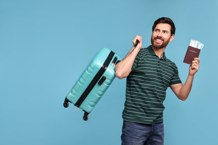 Smiling man with passport, suitcase and tickets on light blue background. Space for textの写真素材