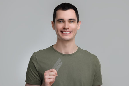 Young man with whitening strips on light gray background