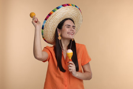 Young woman in Mexican sombrero hat dancing with maracas on beige backgroundの写真素材