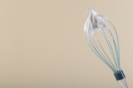 Whisk with whipped cream on beige background. Space for textの写真素材