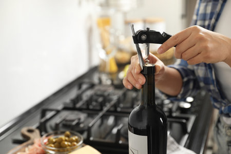 Woman opening wine bottle with corkscrew indoors, closeup. Space for textの写真素材