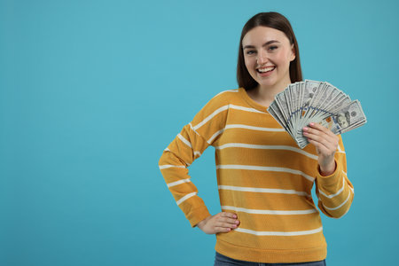 Happy woman with dollar banknotes on light blue background, space for textの写真素材