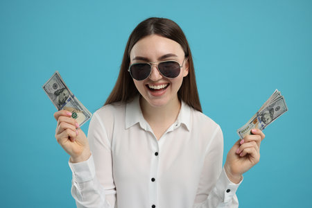 Happy woman with dollar banknotes on light blue backgroundの写真素材