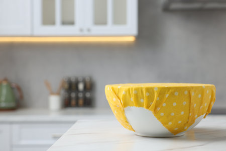 Bowl covered with beeswax food wrap on white table indoors, space for textの写真素材