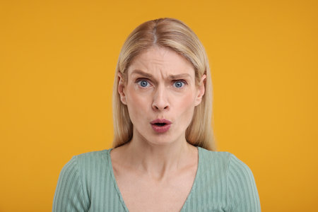 Portrait of surprised woman on yellow backgroundの写真素材