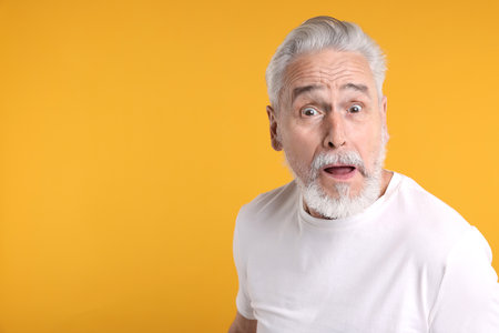 Portrait of surprised senior man on yellow background, space for textの写真素材