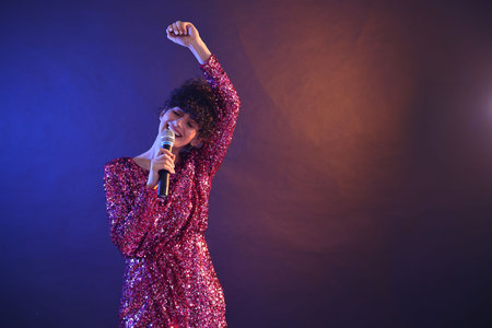 Beautiful young woman with microphone singing on color background in neon lights. Space for textの写真素材