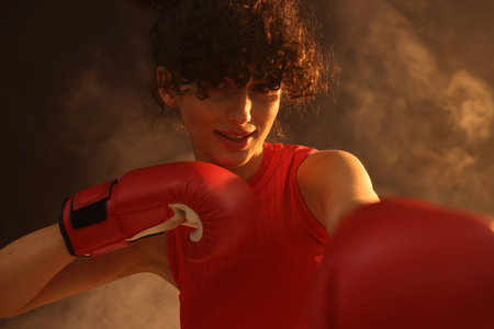 Beautiful young woman with boxing gloves on color background in neon lights and smokeの写真素材