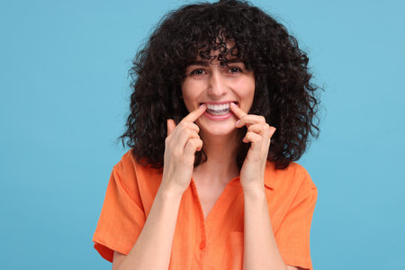 Young woman applying whitening strip on her teeth against light blue background