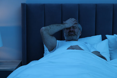 Mature man suffering from headache in bed at nightの写真素材