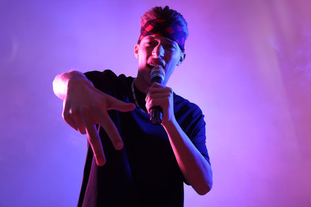 Stylish young man singing on color background in neon lightsの写真素材