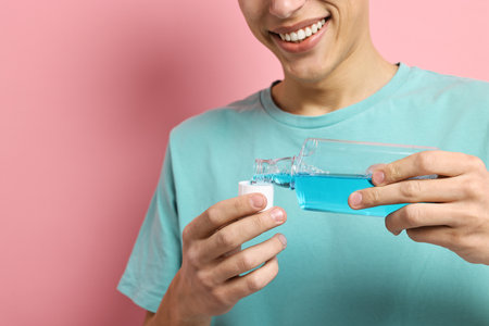 Young man using mouthwash on pink background, closeupの写真素材