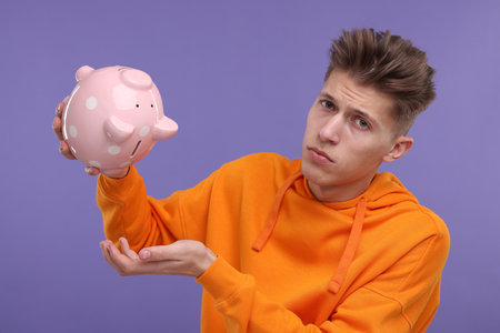 Upset man with piggy bank on purple backgroundの写真素材
