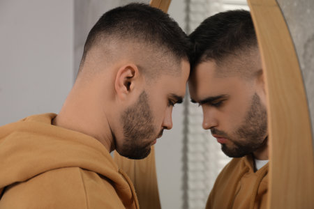 Sad young man near mirror at homeの写真素材