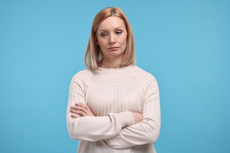 Sad woman with crossed arms on light blue backgroundの写真素材