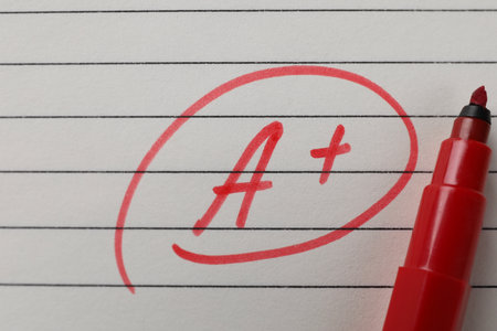 School grade. Red letter A with plus symbol on notebook paper and marker, top view