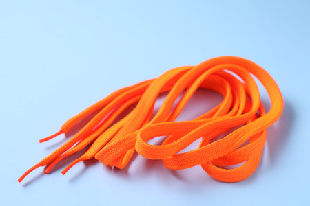 Stylish orange shoe laces on light blue background, closeup