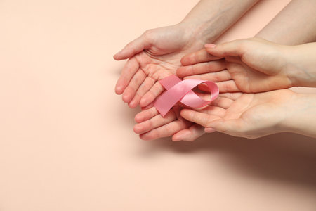 Breast cancer awareness. Women holding pink ribbon on beige background, top view. Space for textの写真素材