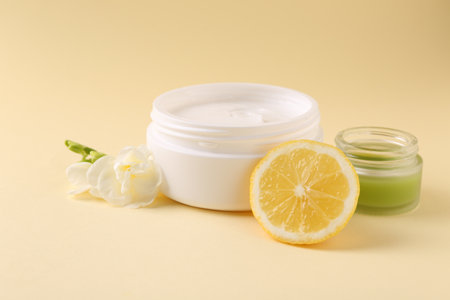 Moisturizing cream in open jars, lemon and freesia flower on beige background. Body care productsの写真素材