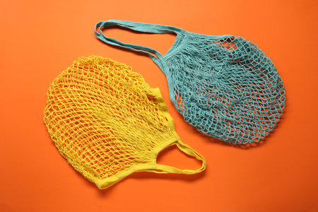 Yellow and turquoise net bags on orange background, top view