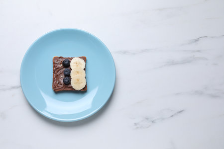 Toast with tasty nut butter, blueberries, banana and nuts isolated on white marble table, top view....