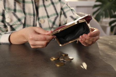 Poor woman pouring coins out of wallet at gray table indoors, closeup