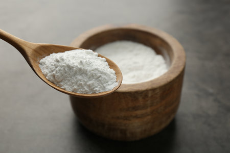 Spoon of baking powder over bowl at gray textured table, closeup. Space for text