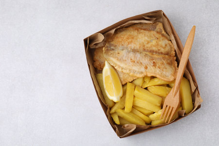 Delicious fish and chips in paper box served on light gray table, top view. Space for textの写真素材