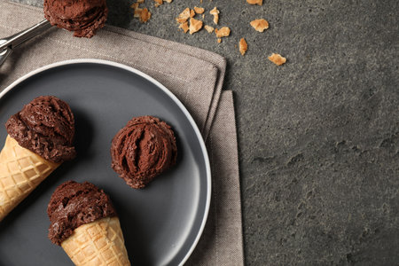 Chocolate ice cream scoops in wafer cones on gray textured table, flat lay. Space for textの写真素材