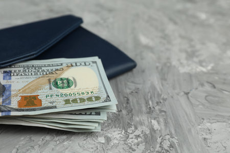 Money exchange. Wallet with dollar banknotes on gray stone background, closeup. Space for text