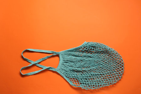 Turquoise net bag on orange background, top view. Space for text